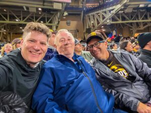 Three men in selfie photo seated in a sports stadium