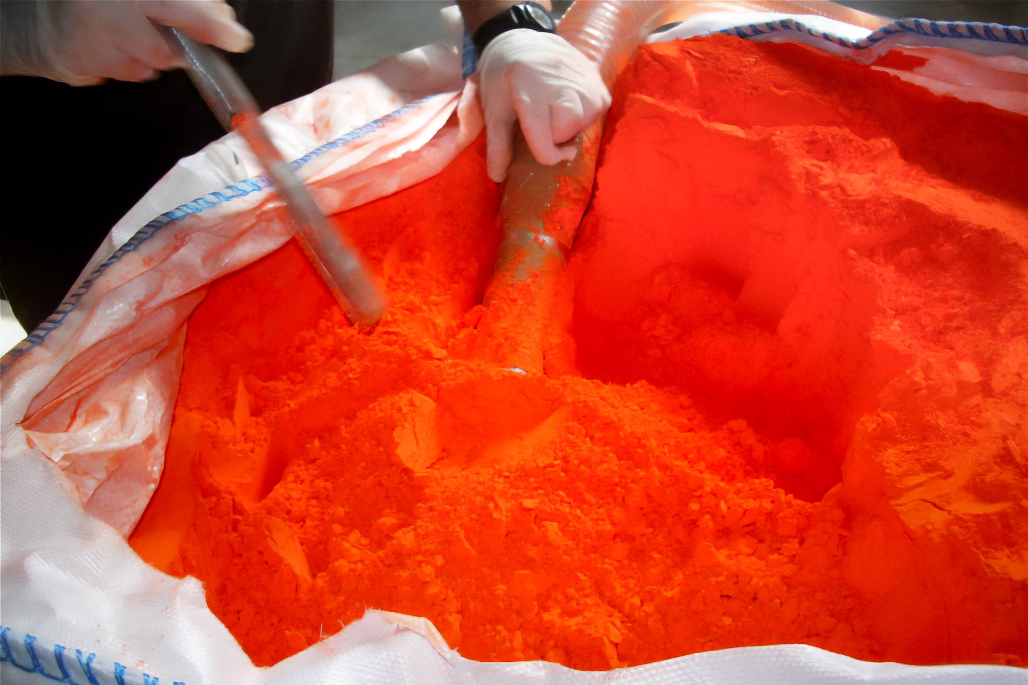 Red Lead powder in a large bag with hands and tools in powder