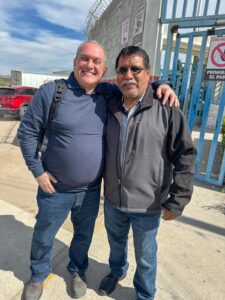 Two men smiling for photo infront of a factory gate