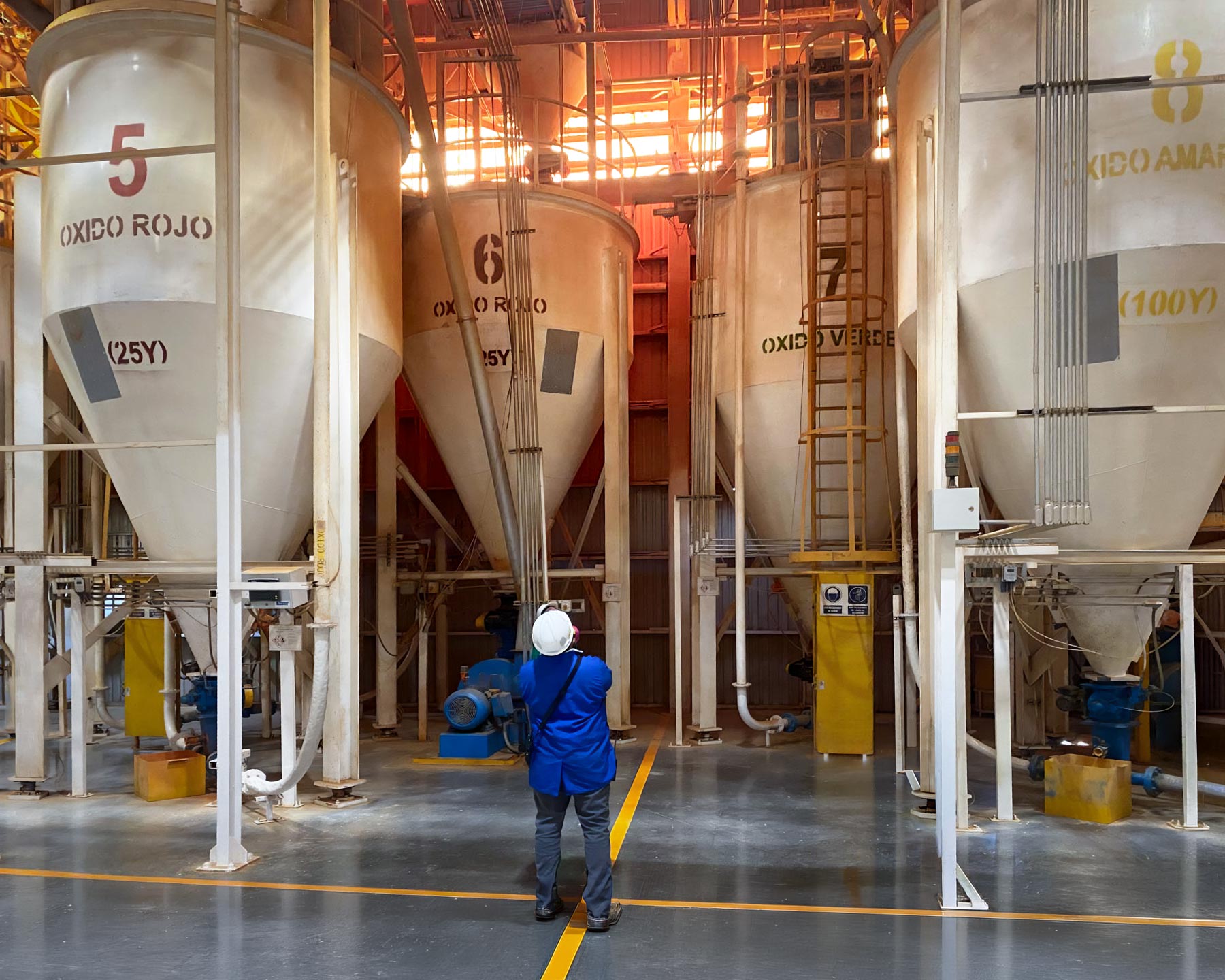 person in hard hat looking up at large silos