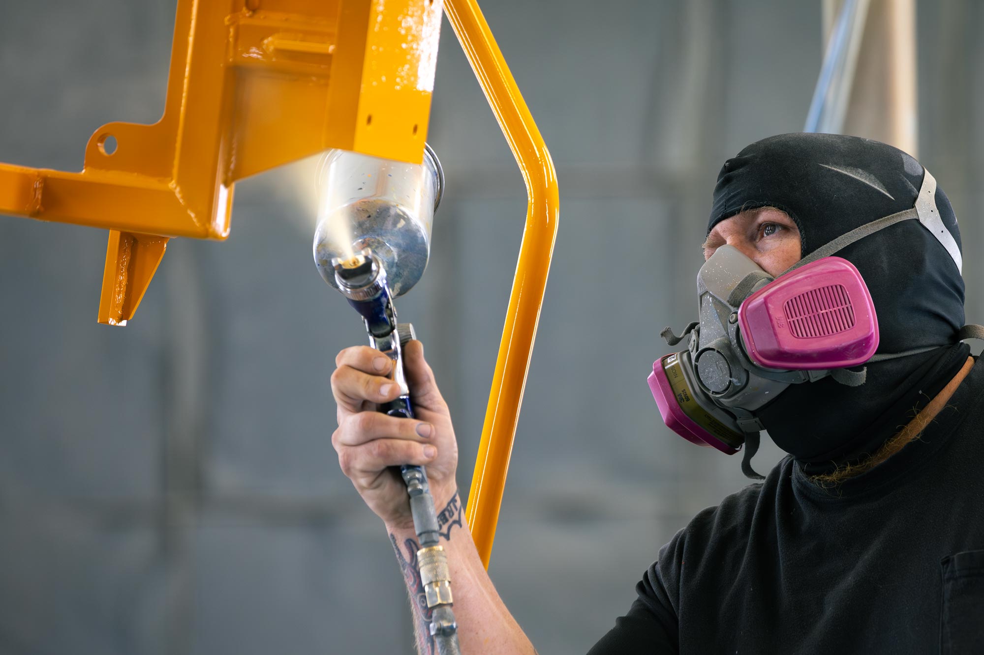 man painting machine parts with spray gun wearing protective face mask