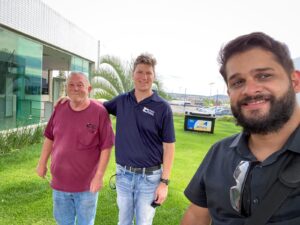 Three men in a selfie photo with a Moura factory sign in the background