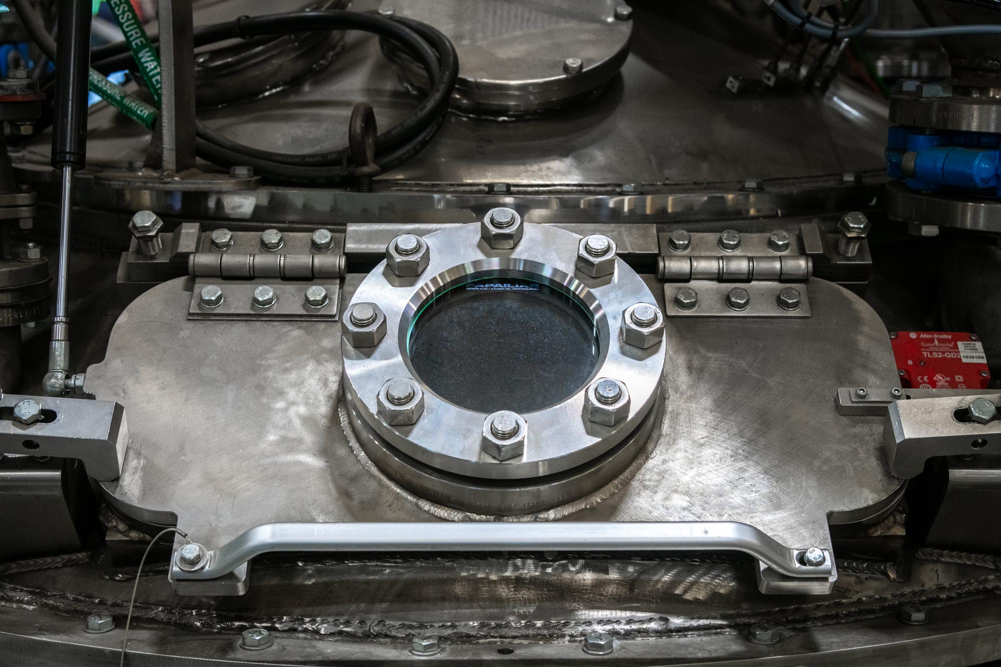 machine detail showing round metal window hatch with bolts around the glass